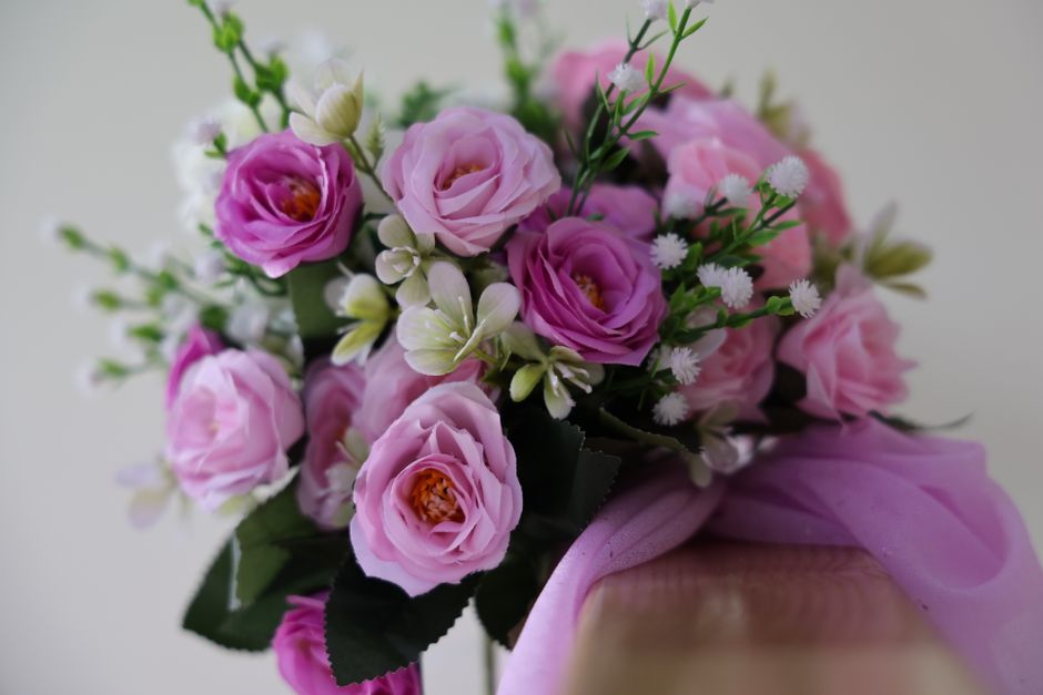 A floral arrangement featuring a bouquet of soft pink roses with tightly layered petals and warm orange centers, complemented by delicate white miniature daisy-like flowers and cream-colored orchid bu